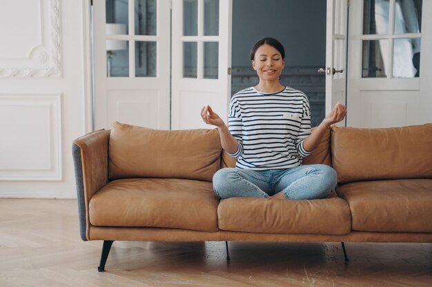 Glimlachende vrouw die yoga beoefent mediteert thuis op de bank Gezonde levensstijl wellness