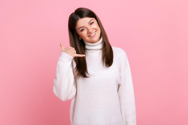 Glimlachende vrouw die zich met gelukkige speelse uitdrukking bevindt die telefoongebaar maakt met hand flirten