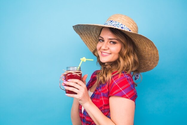 Glimlachende vrouw drinkt rood sap. studio portret met blauwe achtergrond en kopieer ruimte.