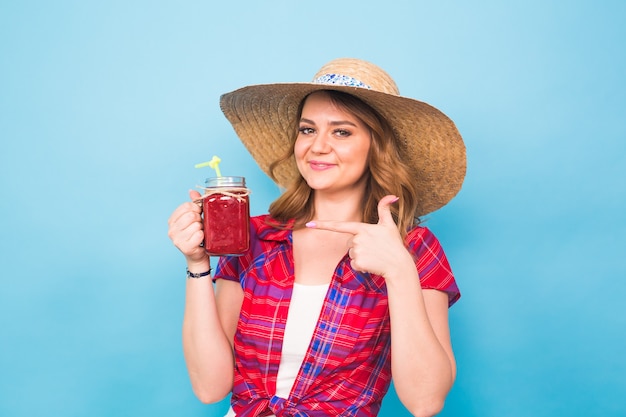 Glimlachende vrouw drinkt rood sap. studio portret met blauwe achtergrond en kopieer ruimte.