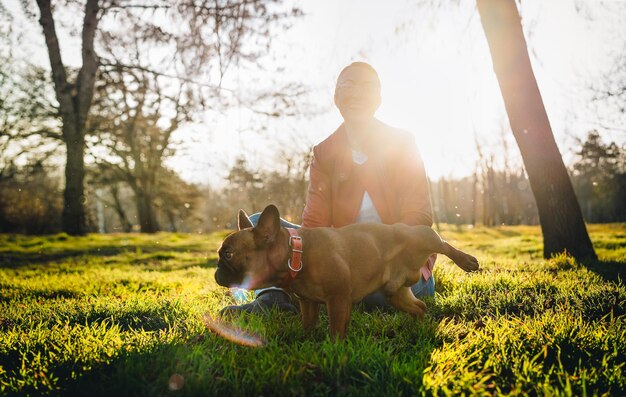 Foto glimlachende vrouw en franse bulldog hond zitten in het gras in het park