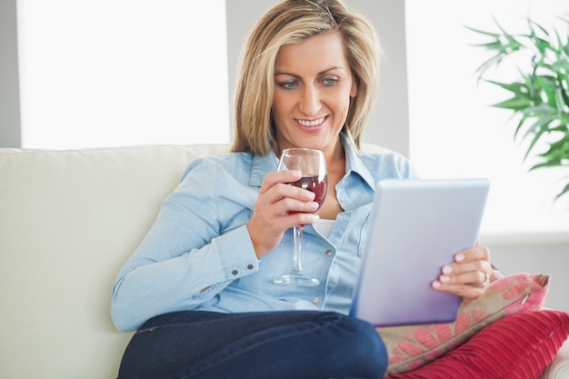 Glimlachende vrouw het drinken wijn en het gebruiken van een tabletpc