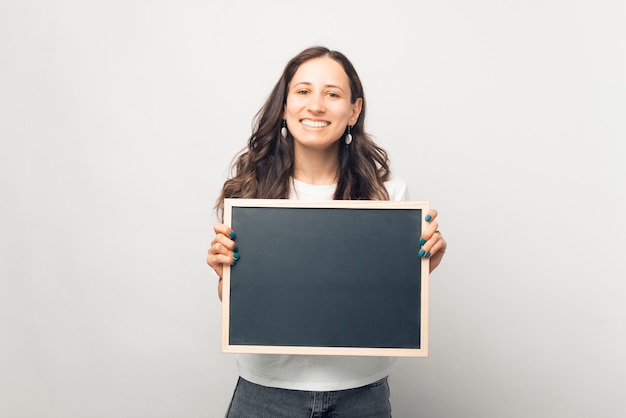 Glimlachende vrouw houdt een klein bord met ruimte voor uw tekst.