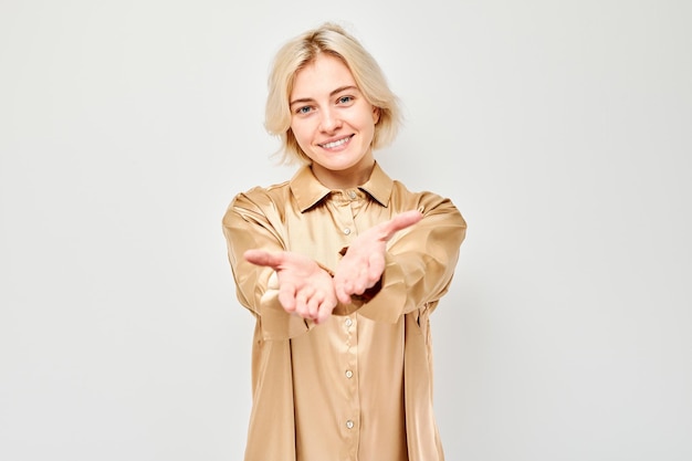 Glimlachende vrouw in een beige hemd die met haar handen op een lichte achtergrond gebaren maakt