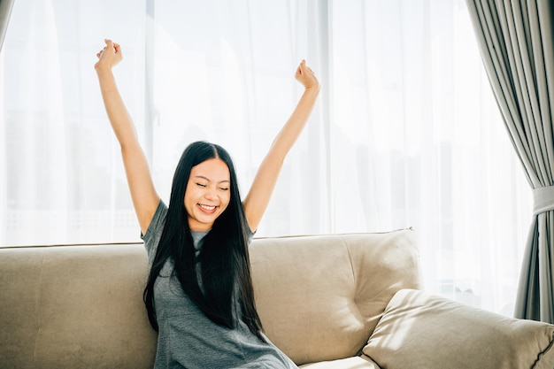 Glimlachende vrouw in een luxe woonkamer tilt haar armen op en strekt zich uit na het zitten