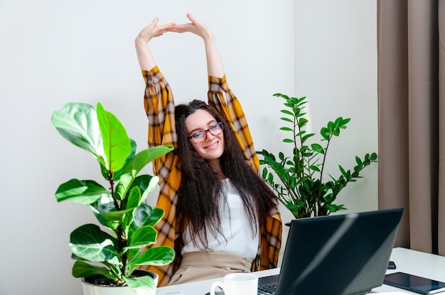 Glimlachende vrouw in glazen die zich uitstrekt op een werkplek vrouw die thuis werkt met behulp van laptopcomputer