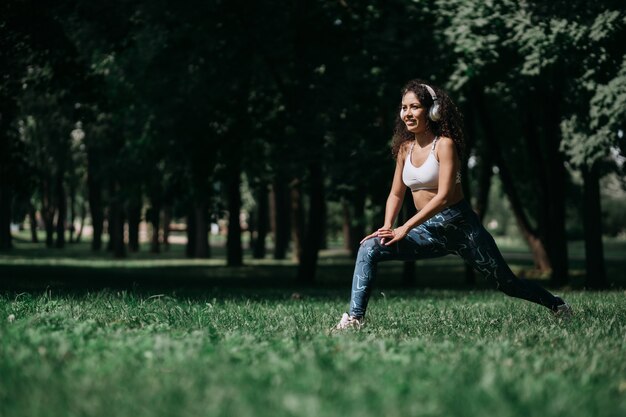 Glimlachende vrouw in hoofdtelefoons die zich uitstrekt voordat ze buiten jogt