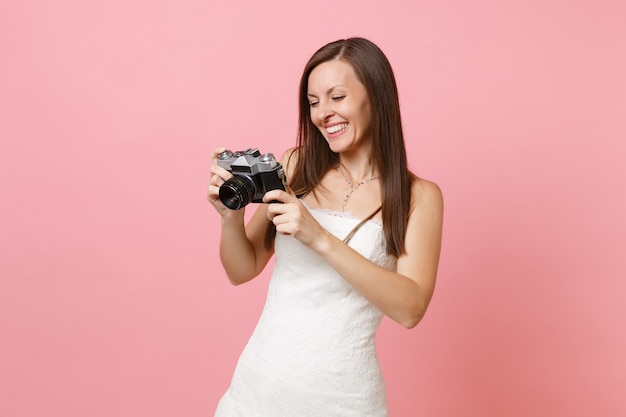 Glimlachende vrouw in witte jurk die op retro vintage fotocamera kijkt en personeelsfotograaf kiest