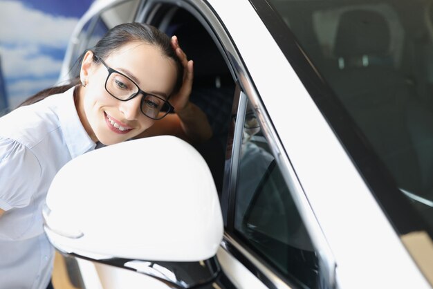 Glimlachende vrouw kijkt in de zijspiegel van auto-positief en auto-aankoopconcept