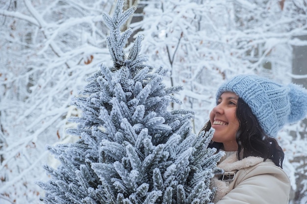 glimlachende vrouw kijkt naar sneeuwige kerstboom in haar handen