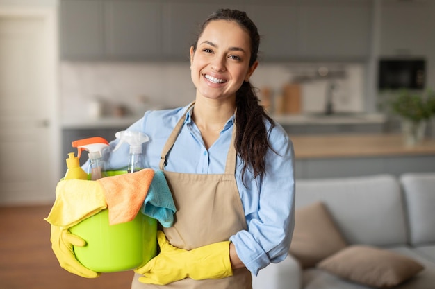 Glimlachende vrouw klaar met een emmer schoonmaakmiddelen