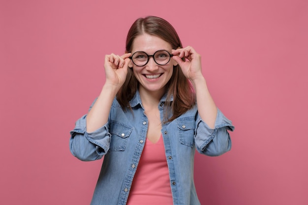 Glimlachende vrouw met bril geïsoleerd op roze studio-opname kijken naar camera Positive