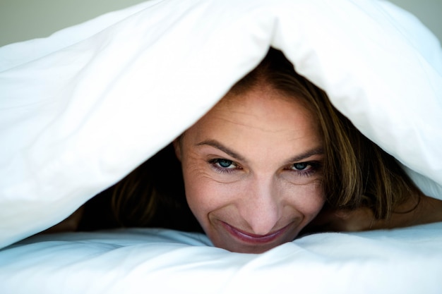 glimlachende vrouw met een dekbed over haar hoofd getrokken