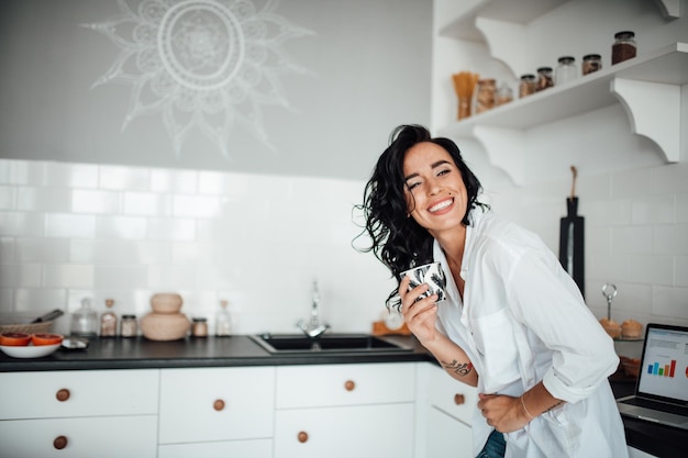 Glimlachende vrouw met een koffiekop in de keuken