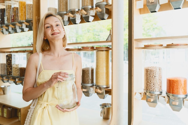 Glimlachende vrouw met een lege glazen pot die winkelt in een duurzame plasticvrije supermarkt