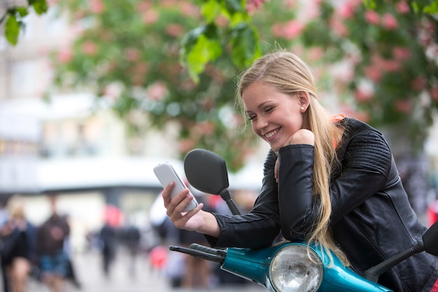 Foto glimlachende vrouw met een mobiele telefoon terwijl ze op een scooter leunt