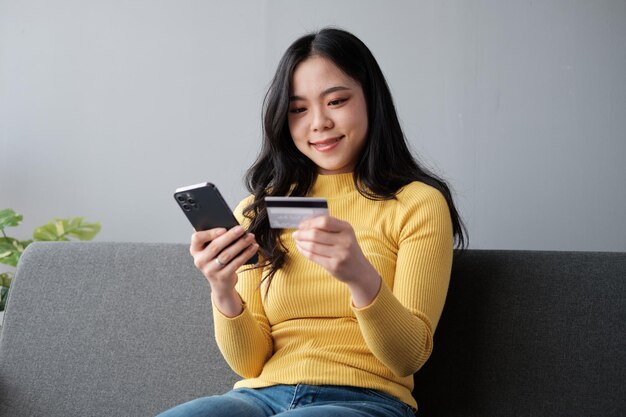 Glimlachende vrouw met een smartphone en een bankkredietkaart die thuis online mobiel winkelt. Gelukkige vrouwelijke shopper die goederen of diensten op het internet koopt.