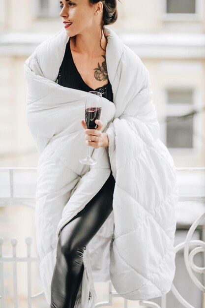 Foto glimlachende vrouw met een wijnglas die een deken draagt terwijl ze in de winter op het balkon staat