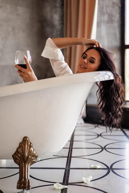 Foto glimlachende vrouw met een wijnglas in de badkuip
