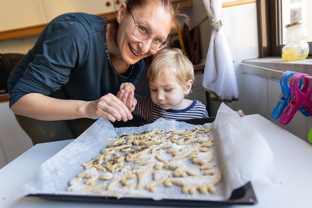 Glimlachende vrouw met haar zoontje maakt koekjes op de keuken in de vorm van dinosaurussen die in t kijken