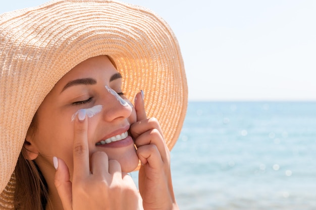 Glimlachende vrouw met hoed brengt zonnebrandcrème aan op haar gezicht in indiase stijl