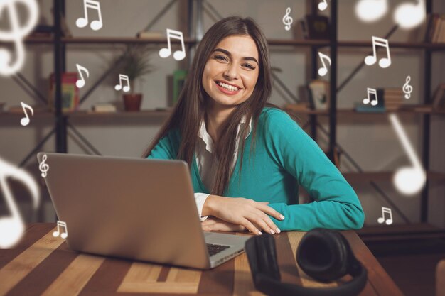 Glimlachende vrouw met koptelefoon zit aan de houten tafel met laptop op tafel