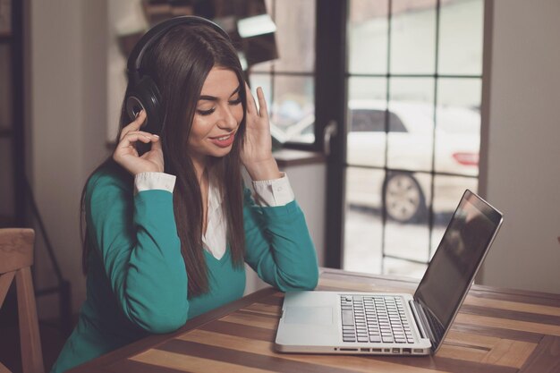 Glimlachende vrouw met koptelefoon zit aan de houten tafel met laptop