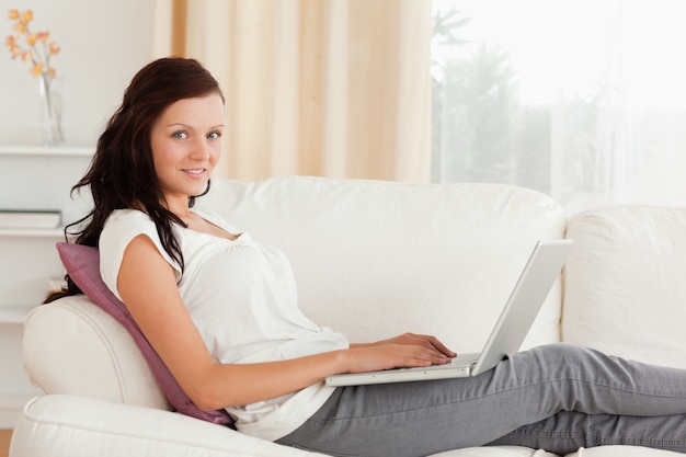Glimlachende Vrouw met laptop die op een bank ligt