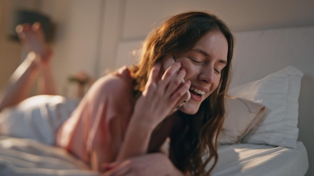 Glimlachende vrouw met mobiele telefoon in bed in het ochtendzonlicht
