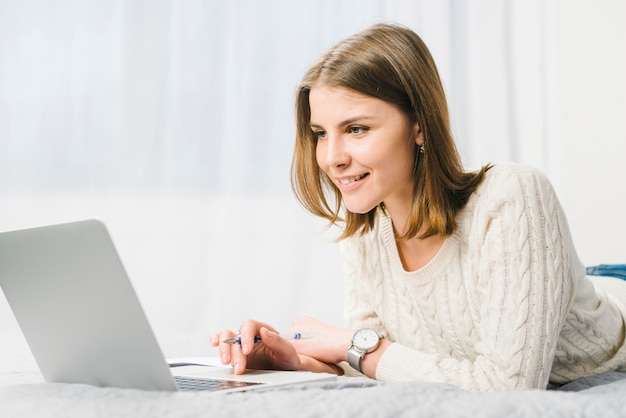 Glimlachende vrouw met pen doorbladerende laptop