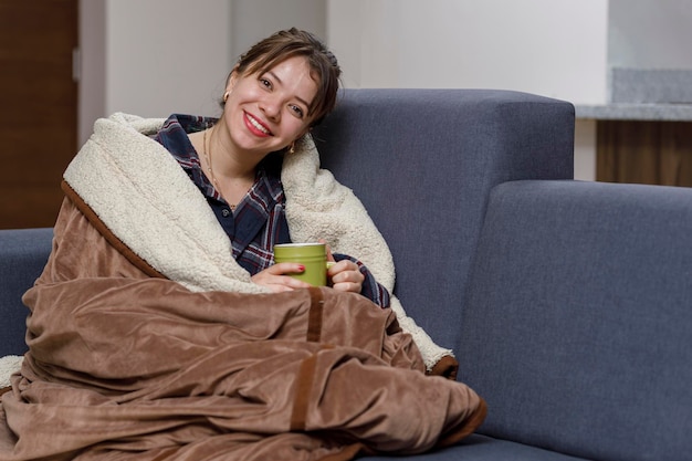 Glimlachende vrouw rustend in een fauteuil bedekt met haar deken voor het koude seizoen