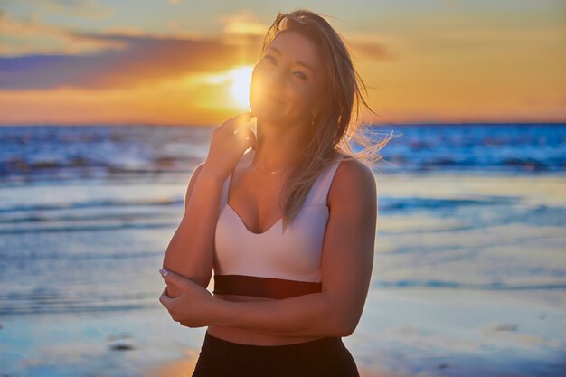 Glimlachende vrouw staat op zomeravond aan zee