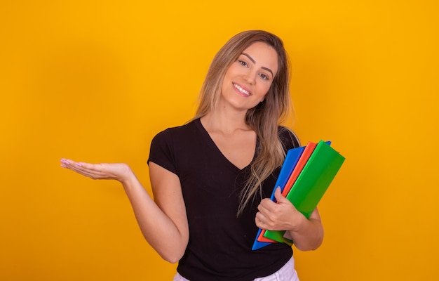 Glimlachende vrouw student met schoolboeken in handen op gele achtergrond