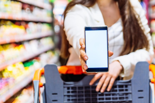 Glimlachende vrouw toont wit scherm op smartphone. boodschappen doen.