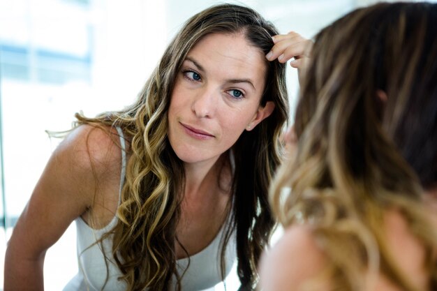 glimlachende vrouw tot vaststelling van haar haren in de badkamerspiegel