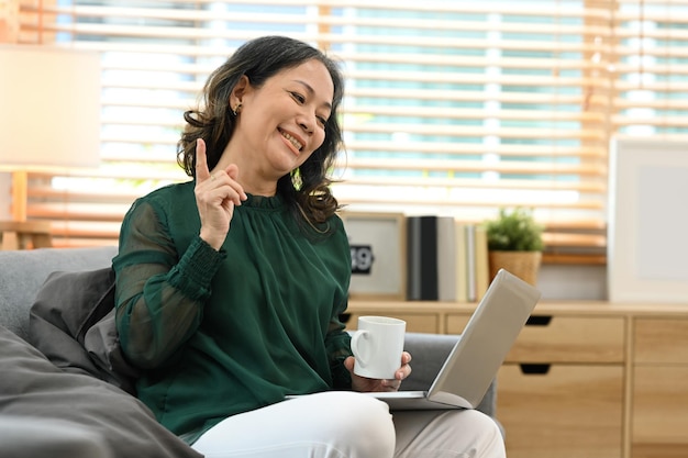 Glimlachende vrouw van middelbare leeftijd die videogesprek voert met virtuele chat op laptop vanuit huis pensioen levensstijl concept