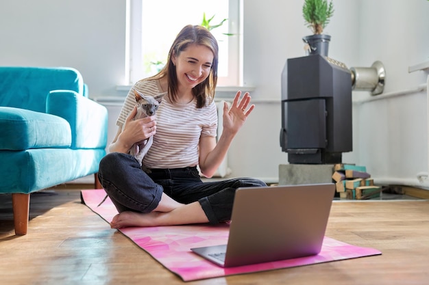 Foto glimlachende vrouw van middelbare leeftijd met laptop en kat op de vloer