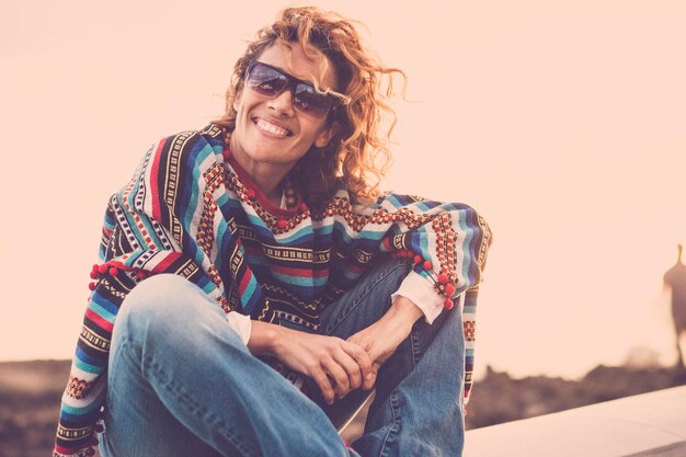 Foto glimlachende vrouw zit op een steunmuur bij de zee tegen de lucht