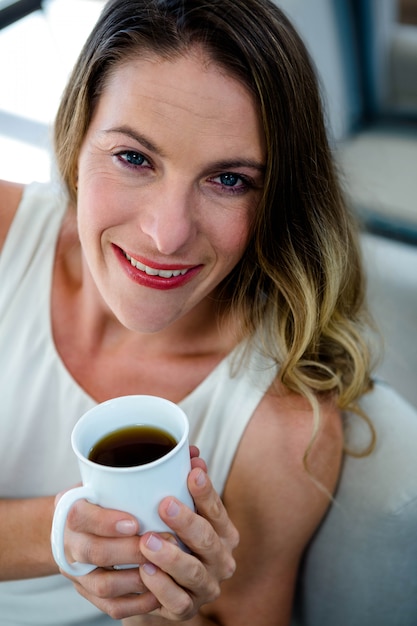 glimlachende vrouw, zittend op de bank, met een kopje koffie