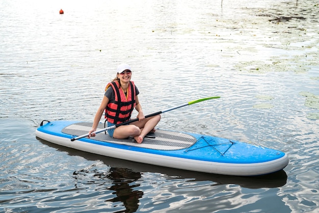 Glimlachende vrouw zittend op sup board met peddel rusten en zonnebaden op een natuur