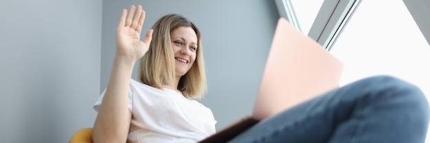 Glimlachende vrouw zwaait met haar hand naar laptop