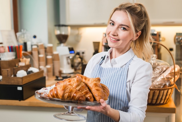 Glimlachende vrouwelijke bakker die gebakken croissant in de caketribune houden