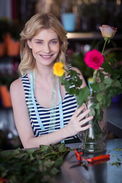 Glimlachende vrouwelijke bloemist die bloemboeket in vaas schikken bij bloemwinkel
