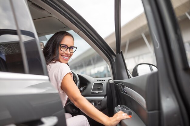 Glimlachende vrouwelijke chauffeur opent de deur van een rechtsgestuurde auto voor een winkelcentrum.