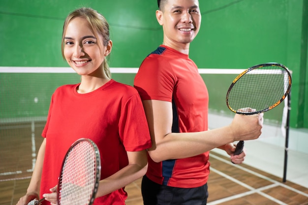 Glimlachende vrouwelijke en mannelijke badmintonspelers die rackets vasthouden