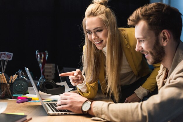 Glimlachende vrouwelijke en mannelijke it-specialisten die laptop op kantoor gebruiken