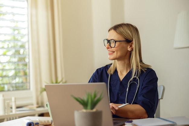 Glimlachende vrouwelijke gezondheidswerker die laptop gebruikt tijdens het werken bij het gezondheidszorgconcept van het artsenkantoor