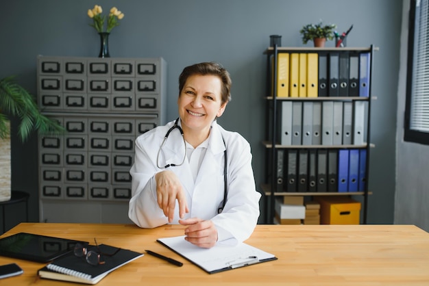 Glimlachende vrouwelijke gezondheidswerker die wat papierwerk doet en laptop gebruikt terwijl ze op het kantoor van de dokter werkt