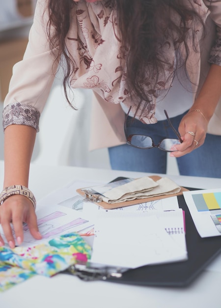 Glimlachende vrouwelijke modeontwerper zit aan een bureau