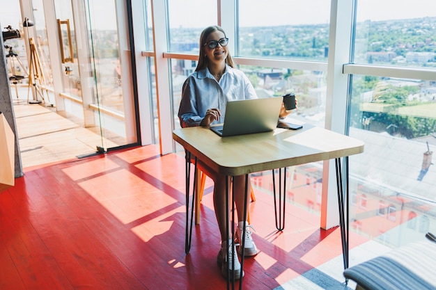 Glimlachende vrouwelijke student in glazen genieten van het kijken naar film online op laptop in vrije tijd in gezellige coworking ruimte gelukkige vrouwelijke freelancer chatten met vriend op sociale media profielfoto's delen